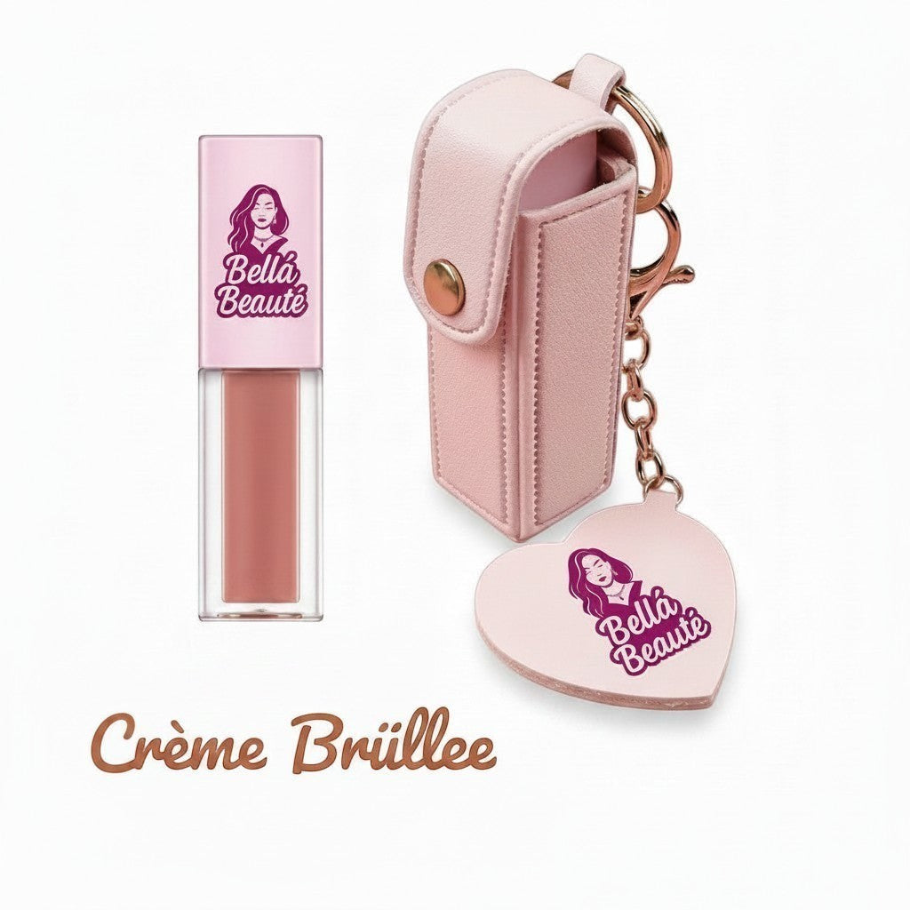 Bella Beauté Crème Brûlée lip oil in a clear tube with a pink cap, attached to a pink leather keychain holder with a heart charm.