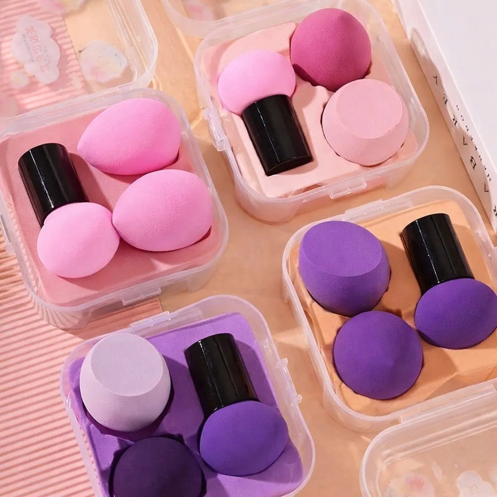 Bella Beauté makeup sponges in pink and purple, featuring teardrop and mushroom shapes with black handles, stored in clear travel cases.